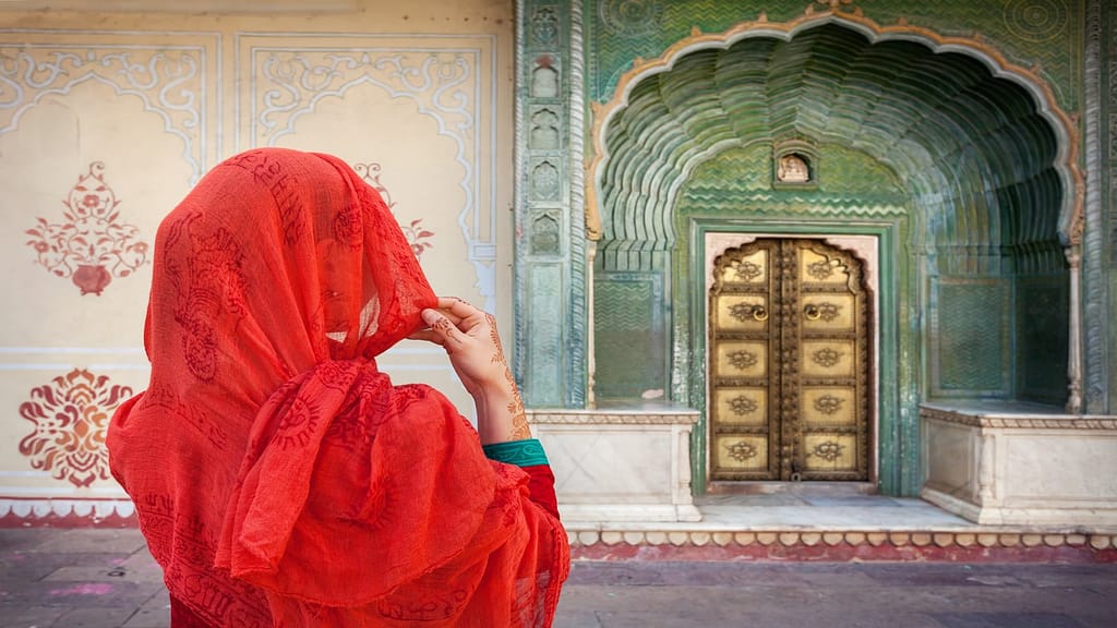 Woman in red scarf looking at green gate door in City Palace of Jaipur, Rajasthan, India