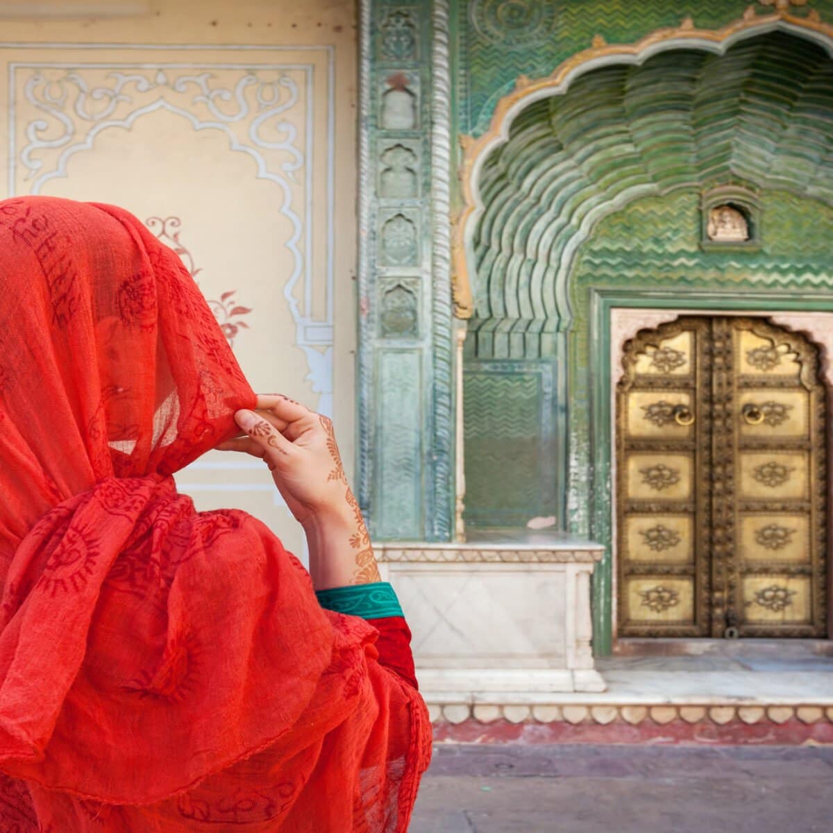 Woman in red scarf looking at green gate door in City Palace of Jaipur, Rajasthan, India