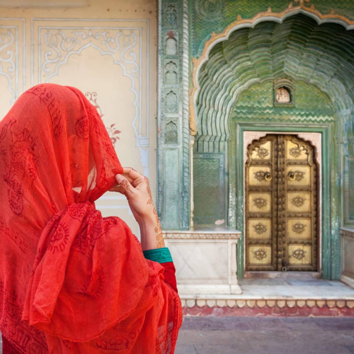 Woman in red scarf looking at green gate door in City Palace of Jaipur, Rajasthan, India